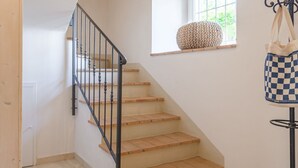 Un escalier avec des marches en bois et une rampe noire, une fenêtre ornée d’un panier tressé et un sac à carreaux suspendu à un présentoir.