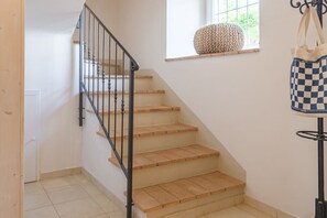 A staircase with wooden steps and a black railing, a window with a woven basket, and a checkered bag hanging on a stand.