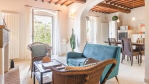 Un vaste espace de vie comprenant un canapé bleu, des fauteuils en osier, une table à manger et, au fond, une cuisine.