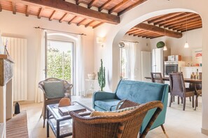 Un vaste espace de vie comprenant un canapé bleu, des fauteuils en osier, une table à manger et, au fond, une cuisine.