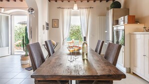 Un coin repas rustique avec une table en bois, des chaises en osier et une bouteille de vin.