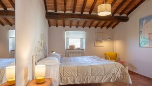 Une chambre à coucher avec un grand lit, une chaise, une petite table, une fenêtre et un tableau accroché au mur.