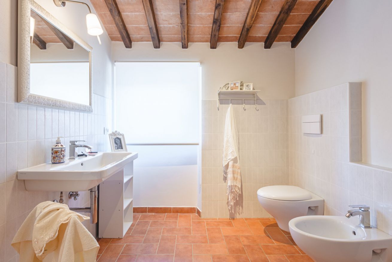 Une salle de bain équipée d’un lavabo, de toilettes et d’un bidet, avec des poutres en bois au plafond et une fenêtre.