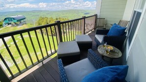 Un balcon agrémenté de meubles en osier, une petite table avec des boissons, et une vue sur un paysage verdoyant et un bâtiment situé au loin.