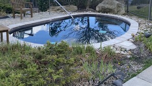 Une piscine avec une terrasse en bois, un banc et un escalier en métal.