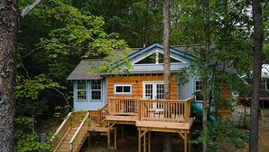 A cabin with a wooden deck, a staircase, and a green slide. - 2-story treehouse with a cargo net connecting the upstairs lofts, a large balcony with a slide to the ground level, sleeps 10. (Mill Spring)