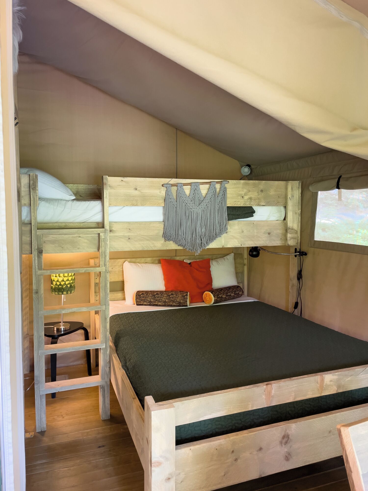 A bunk bed with a macrame wall hanging, a lamp, and a log on the shelf.