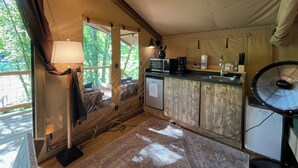 Une cuisine compacte équipée d’un four à micro-ondes, d’une machine à café et d’un évier. On y trouve également un ventilateur et une fenêtre avec des rideaux.