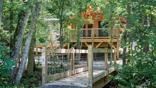 Un pont en bois mène à une structure en bois à plusieurs niveaux, entourée d’arbres.
