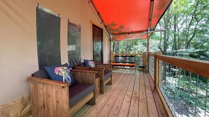Une terrasse en bois couverte, dotée de sièges et offrant une vue sur la forêt.