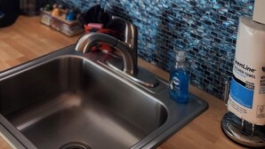 A modern kitchen with a stainless steel sink, a blue mosaic backsplash, and a welcome sign for EmberGlow Outdoor Resort. - 30' Yurt with a large deck, on the creek, full kitchen, dome skylight, 2 bedrooms, sleeps 5. (Mill Spring)