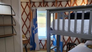 A room with a bunk bed, wooden flooring, a desk with shelves, and a window with curtains. - 30' Yurt with a large deck, on the creek, full kitchen, dome skylight, 2 bedrooms, sleeps 5. (Mill Spring)