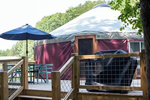 Een joert met een overdekt terras, een barbecue en een houten omheining.