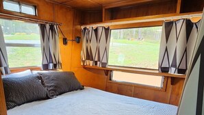 A spacious RV bedroom with a large bed, wooden walls, and windows with curtains. - Vintage 1955 Imperial Mansion, deck on the creek, easy access to pool and playground, sleeps 5. (Mill Spring)