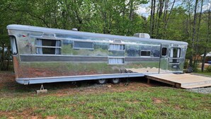 A vintage camper with a small deck, windows, and a kitchenette. - Vintage 1955 Imperial Mansion, deck on the creek, easy access to pool and playground, sleeps 5. (Mill Spring)