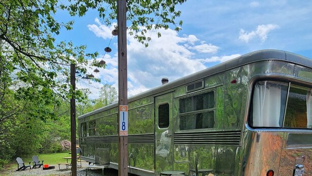 A vintage camper parked in a wooded area with picnic tables and a grill. - Vintage 1955 Imperial Mansion, deck on the creek, easy access to pool and playground, sleeps 5. (Mill Spring)
