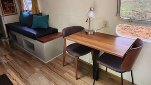Een compact interieur met een bank, tafel en stoelen, een lamp en een raam met uitzicht op de omgeving.