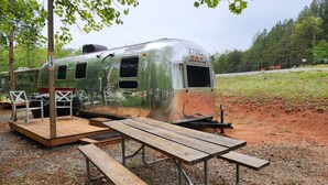 Een oude camper met een picknicktafel en stoelen in een bebost gebied.