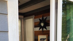 Une porte-fenêtre coulissante donne sur un salon accueillant, où l’on trouve un canapé gris, un coussin orange et un panneau décoratif avec l’inscription « Tennessee ».