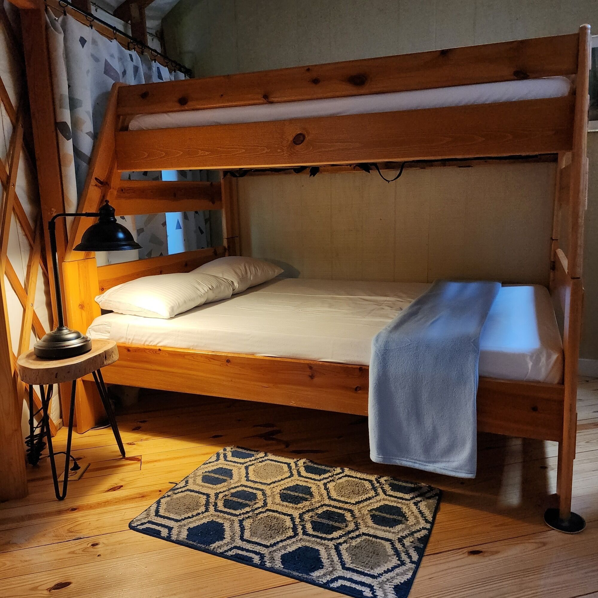 A bunk bed with a wooden frame, a bedside lamp, a patterned rug, and a blanket on the lower bunk.