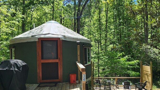A small, single-story cabin with a porch, a covered grill, and a deck with outdoor seating. - 16' Yurt, Dog Friendly, Deck, Dome Skylight, Sleeps 2. (Mill Spring)