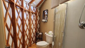 A compact, wooden-framed bathroom with a shower, toilet, and a small shelf. - 16' Yurt, Dog Friendly, Deck, Dome Skylight, Sleeps 2. (Mill Spring)