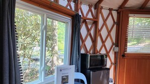 A compact room with a table and chairs, a microwave, and a door leading outside. - 16' Yurt, Dog Friendly, Deck, Dome Skylight, Sleeps 2. (Mill Spring)
