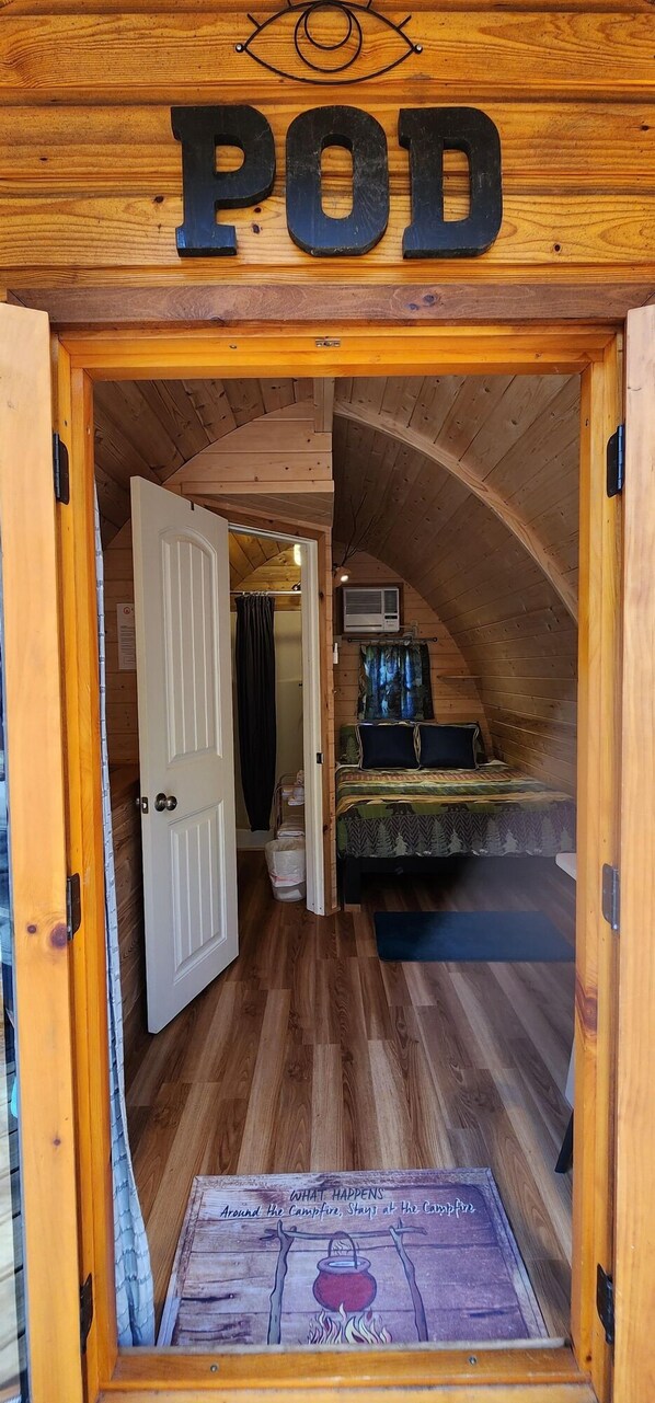 Een gezellig houten blokhut met een slaapkamer op een entresol, met een bed, een klein tafeltje en een raam.