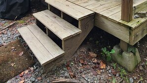 En kuppelformet konstruktion i træ med en trädør og trapper, der fører til en træterrasse.
