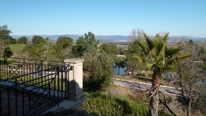 A view from a balcony with a railing, overlooking a landscape with trees, a body of water, and distant mountains. - Séjour inoubliable en Provence | Maison + jardin (Roquebrune sur Argens)