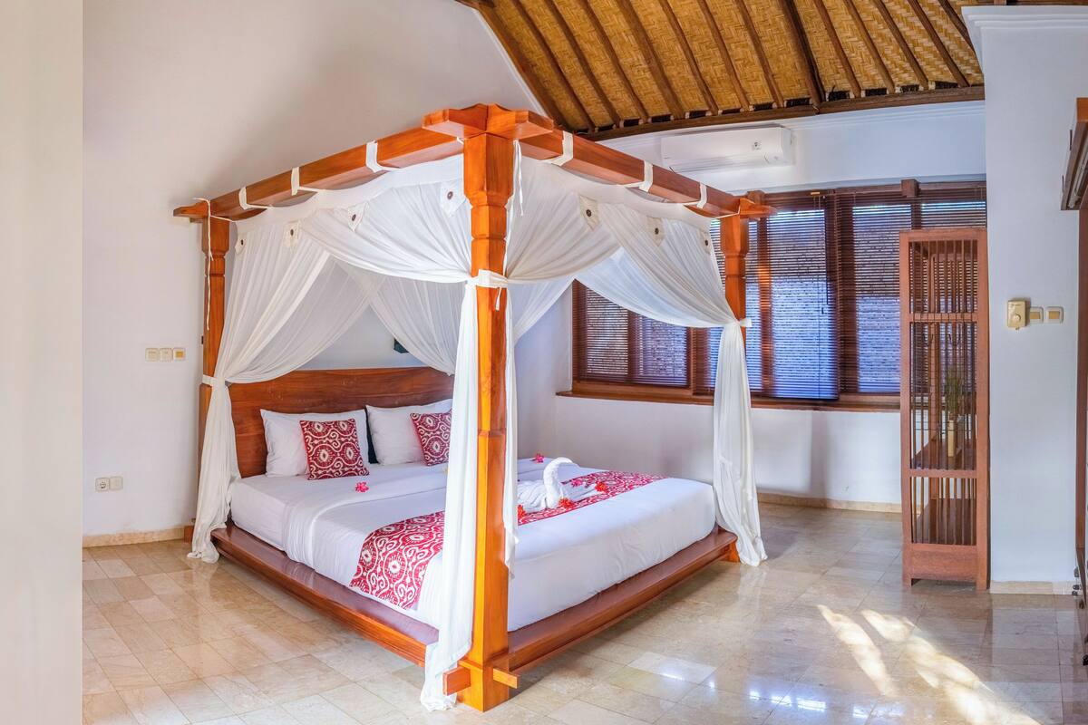 Una cama con dosel, ropa blanca y detalles rojos, un cabecero de madera y un dosel.