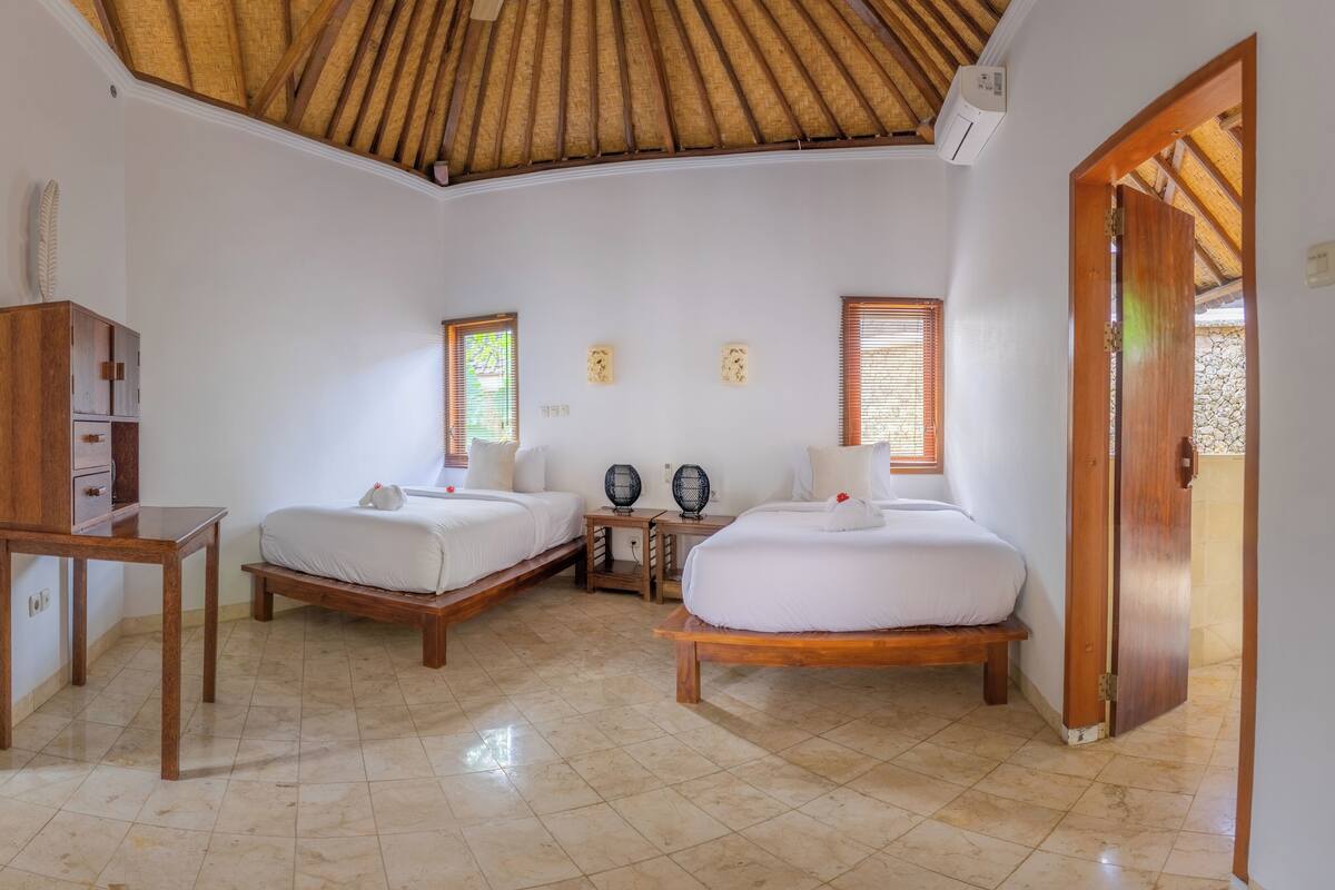 Una habitación con dos camas, un armario de madera, una mesita pequeña y un ventilador de techo.