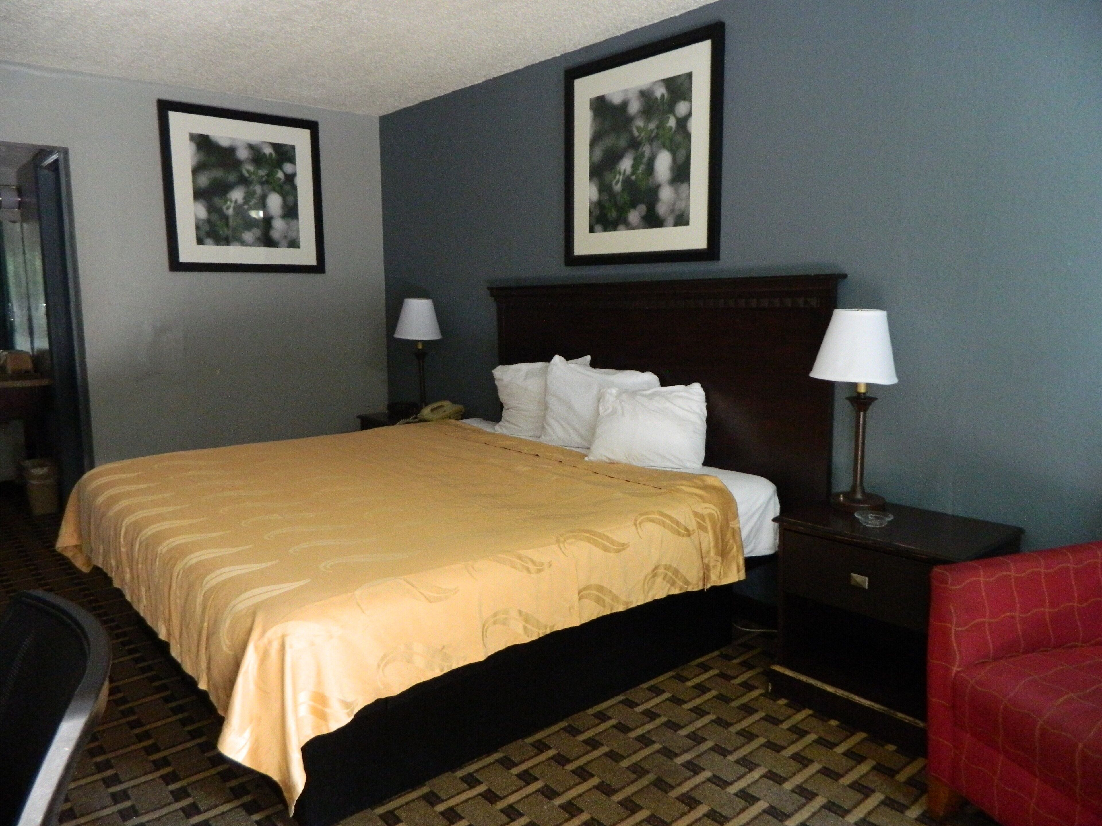 A hotel room with a bed, two bedside tables with lamps, a chair, and two framed pictures on the wall.