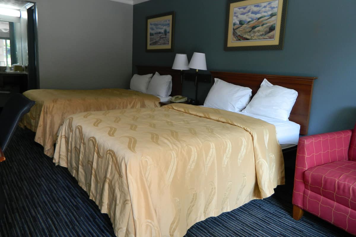 Une chambre d’hôtel avec deux lits, un bureau, une chaise et deux tableaux au mur.