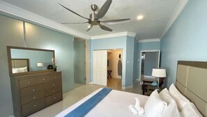 Ein Hotelzimmer mit Bett, Kommode, Spiegel, Deckenventilator und Blick ins Bad.