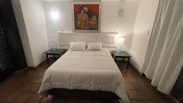 Un dormitorio con una cama, dos mesitas de noche, un aparador, un cuadro en la pared y una ventana con cortinas.