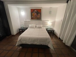 Un dormitorio con una cama, dos mesitas de noche, un aparador, un cuadro en la pared y una ventana con cortinas.