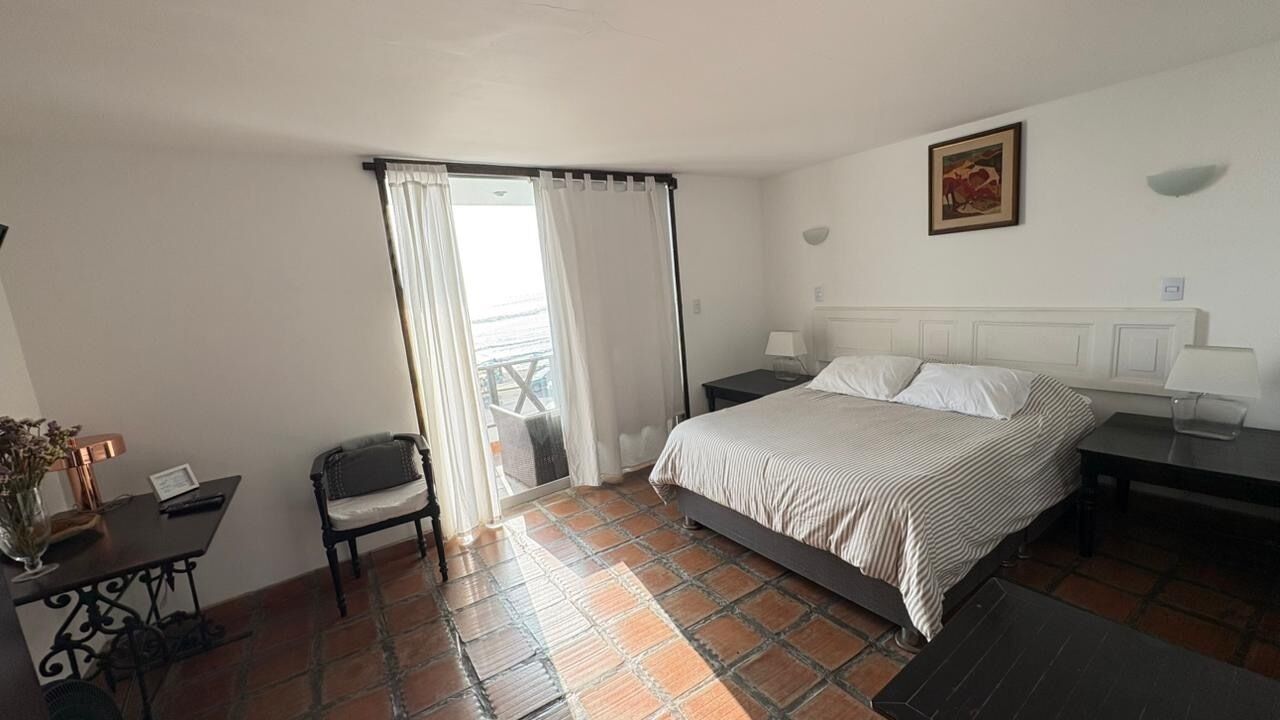 Een hotelkamer met een bed, een bureau, een stoel, een raam met gordijnen en een klein balkon.