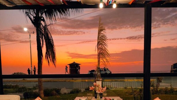 A dining area with a sunset view, a wooden table set with plates and glasses, and blue and red striped cushions.