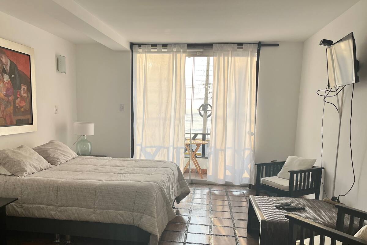 A bedroom with a bed, a desk, a chair, a lamp, and a painting on the wall.