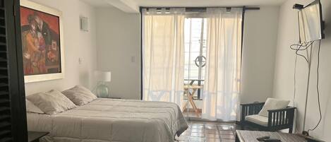 Un dormitorio con cama, escritorio, silla, lámpara y un cuadro en la pared.