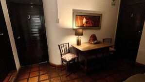 A small room with a wooden door marked with the number 3, a table with a lamp, a chair, and a framed picture on the wall.