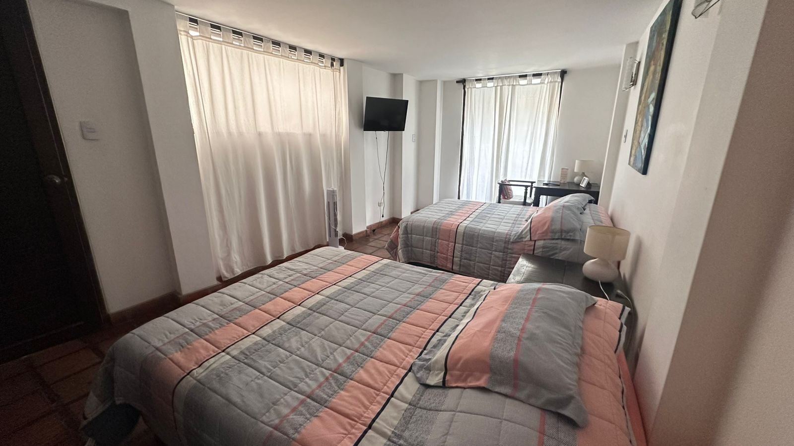A hotel room with two beds, a flat-screen TV, a desk with a chair, and a window with curtains.