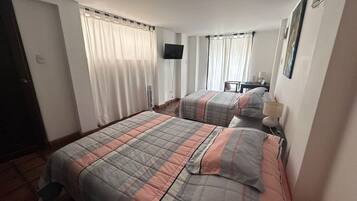 Habitación de hotel con dos camas, un televisor de pantalla plana, un escritorio con silla y una ventana con cortinas.