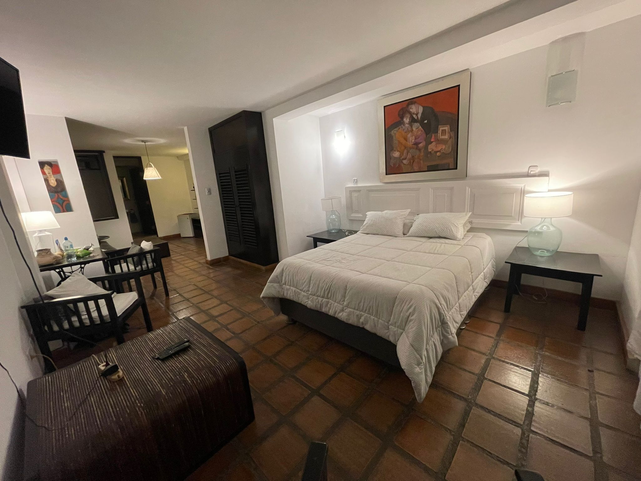 Habitación de hotel con cama, mesitas de noche, escritorio y silla, y un cuadro en la pared.