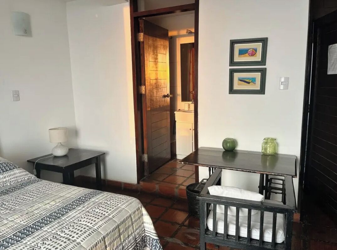 Une chambre d’hôtel avec un lit, une petite table avec une lampe, une chaise et un bureau agrémenté d’un vase.