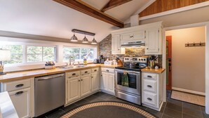 A modern kitchen with white cabinetry, a stainless steel dishwasher, a double oven, and a stone backsplash. - Four Bear Falls (Banner Elk)