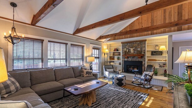 A cozy living room with a fireplace, wooden beams, and a stone wall. - Four Bear Falls (Banner Elk)