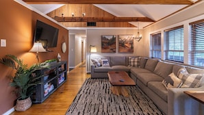 A living room with a wooden ceiling, a sofa, a coffee table, a TV, and a bookshelf. - Four Bear Falls (Banner Elk)
