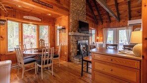 L’intérieur chaleureux d’un chalet avec des murs en bois, une cheminée en pierre, un coin repas avec des chaises et un comptoir de cuisine.